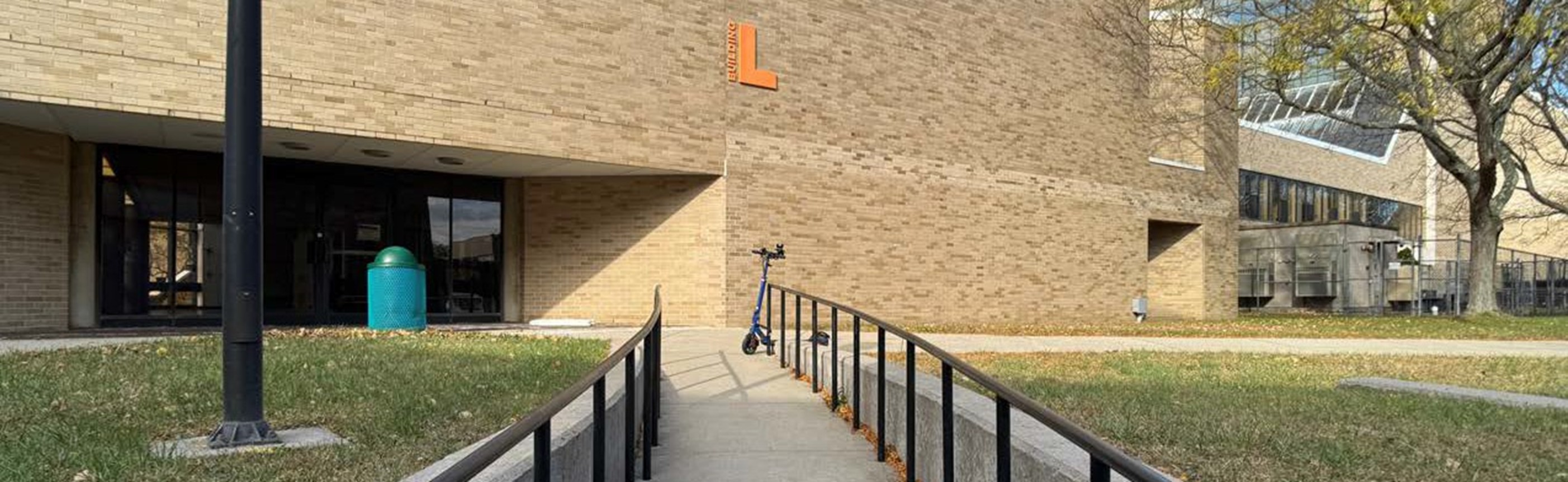 Photo of a ramp outside of one of the Library building entrances with a big, orange letter L on the bulding.