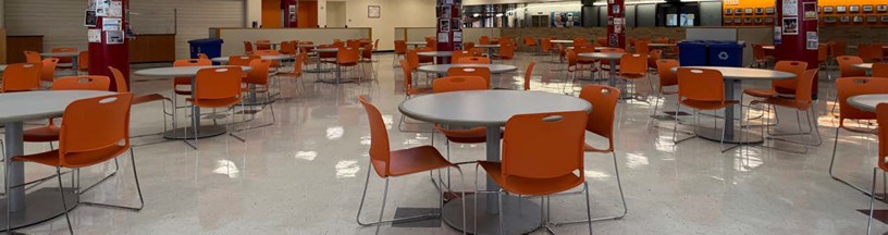 Photo of the student cafeteria seating area with round tables and orange chairs.