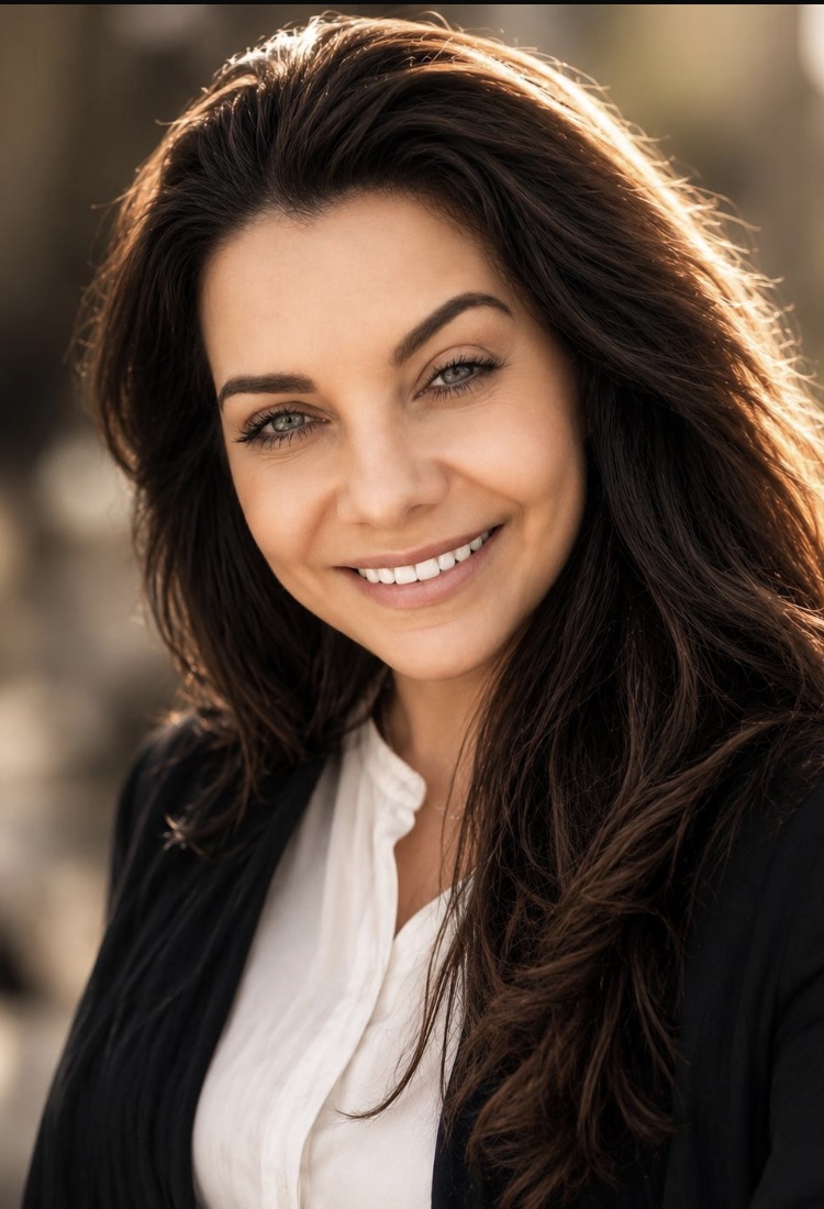 Young woman with long dark hair, wearing a white button-down and a black blazer, smiling at the camera