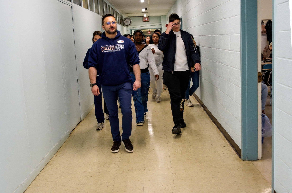 A group of people walking through a hallway with a man in a College Now hoodie in the front