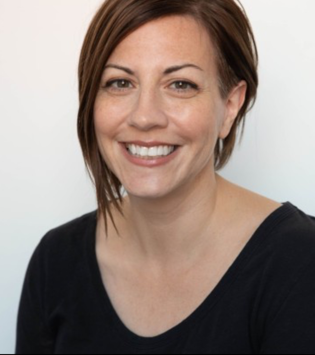 Photo of a woman with short brown hair, wearing a black v-neck shirt, smiling at the camera.