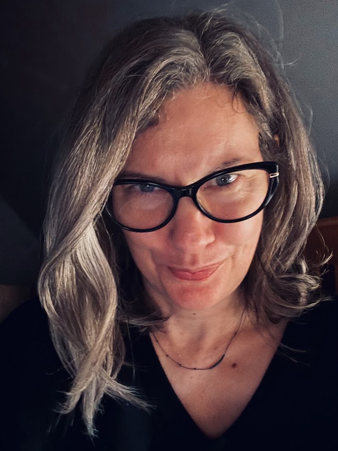 Photo of a woman with shoulder length hair and black framed glasses, wearing a black v-neck top, slightly smiling and looking directly at the camera.